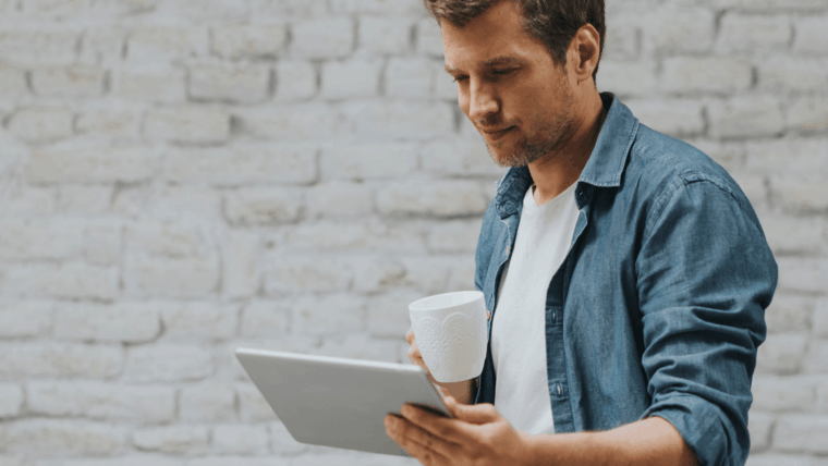 Ein Mann schaut entspannt auf sein Tablet, mit einem Kaffee in der Hand