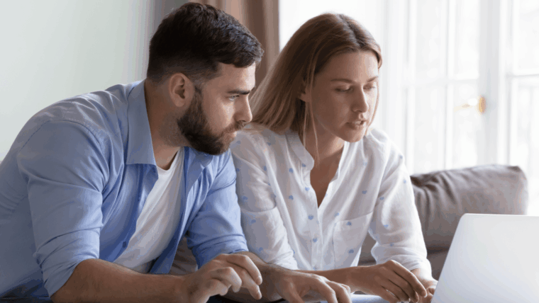 Pärchen sitzt auf der Couch vor Taschenrechner und Laptop und bespricht Finanzen.