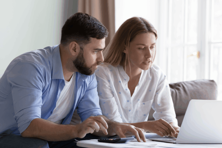 Pärchen sitzt auf der Couch vor Taschenrechner und Laptop und bespricht Finanzen.